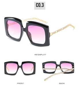 Detail of oversized square sunglasses with black frames and gold chain temples