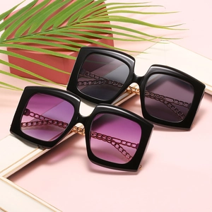 Square cat-eye sunglasses for women with golden metal chain temples on a pink background