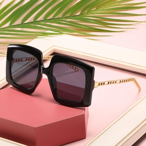 Black square cat-eye sunglasses with gold metal chain temples on pink display stand