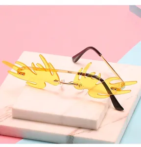 Detail der gelben flammenförmigen randlosen Sonnenbrille mit Goldbügeln auf Marmor