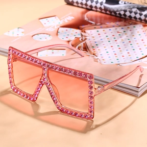 Oversized square sunglasses with pink rhinestones and gradient lenses on a magazine