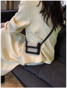 Detail of handmade contrast mini pearl bag worn over a beige blazer by a model