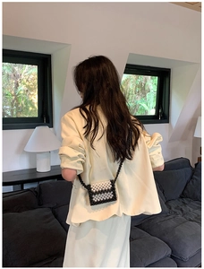 Detailed back view of a black and white woven pearl crossbody bag on a female model