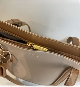 Detailed close-up of golden zipper and WWTU logo on a beige and brown shoulder bag