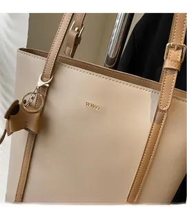 Detail of beige leather tote bag with gold logo and elephant charm accessory