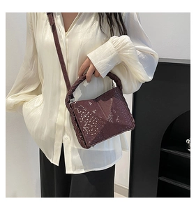 Detail of snake-textured dark purple handbag featuring a unique woven handle and flap cover