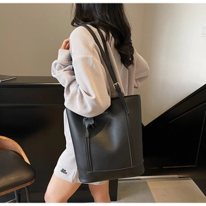 Detail of a black minimalist leather bucket bag with slim shoulder strap and metal buckle