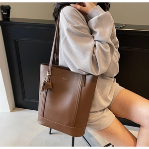 Detail of deep brown leather bucket bag with gold logo and tassel on a beige outfit