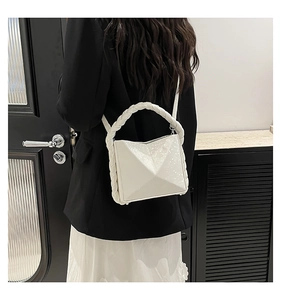 Detail of white handbag with geometric texture and woven handle shown on model