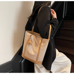 Detail of a beige and brown color-block tote bag with a leather elephant charm accessory