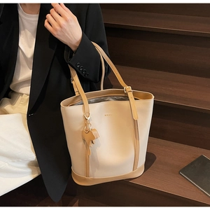 Detail of minimalist cream bucket bag with brown handles and small elephant charm accessory