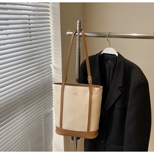 Detail of minimalist cream leather bucket bag with brown contrast trim and metal buckle