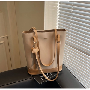 Detail of minimalist cream and brown tote bag with elephant charm on a leather surface
