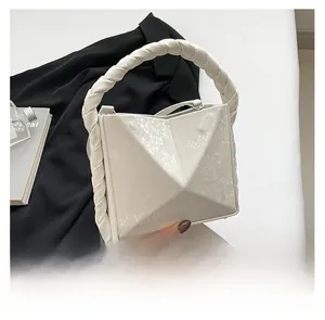 Close-up of white geometric pyramid bag with crocodile texture and woven handle detail