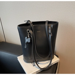 Detail of black PU leather bucket bag with elephant charm and WWTU logo on a book