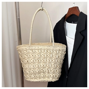 Detailed texture of hand-woven cream straw tote bag hanging on a display stand