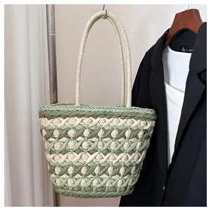 Detail of woven straw tote bag featuring green and beige diamond texture and long handles