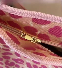 Macro detail of gold metal zipper and pink leopard print canvas on a shoulder bag