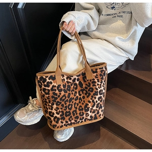 Detail of the leopard print canvas tote bag carried by a model on wooden stairs