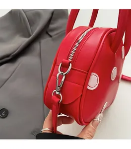 Détail latéral du sac en cuir rouge avec fermeture éclair argentée et anneau en D