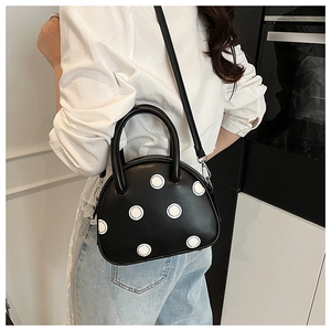 Sac à pois noir et blanc porté en bandoulière avec détail du fermoir métallique