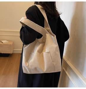 Detail of beige corduroy tote bag showing ribbed texture and front pocket with metal rivets