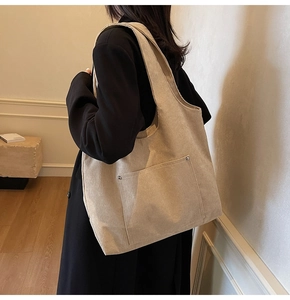 Side view of model wearing a large beige corduroy tote bag with dual front rivet details