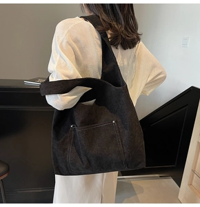 Detail of black corduroy tote bag showing contrast stitching and silver rivets on the pocket