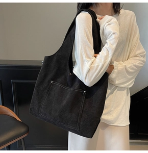 Detail shot of black corduroy tote bag featuring white contrast stitching and metal rivets