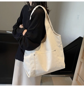 Detail of off-white corduroy tote bag featuring silver rivet pocket and wide shoulder strap