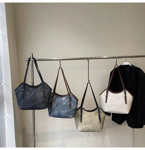 Détail de quatre cabas marbrés en gris, bleu et beige suspendus sur un support métal