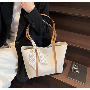 Close-up of cream tote bag with brown straps and geometric silk scarf detail