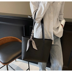 Detail of a black textured tote bag with a checkered silk scarf on a fashion model