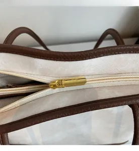 Close-up of smooth gold zipper and brown leather trim on a canvas tote bag