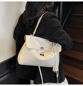 Detail of a creamy white glossy leather tote bag with silver twist lock on black blazer