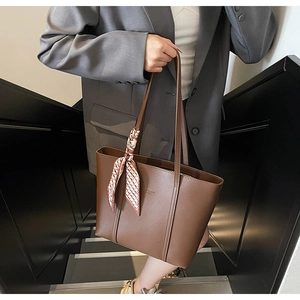 Detail of dark brown leather tote bag with red plaid silk scarf on the handle