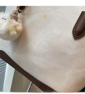 Detail of soft cream suede tote bag with brown leather trim and a plush ball charm