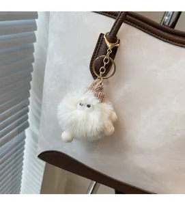 Close-up of white plush keychain with a brown knit hat hanging on a canvas tote bag