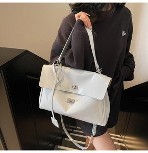 Detail of glossy white tote bag featuring silver twist lock and minimalist flap design