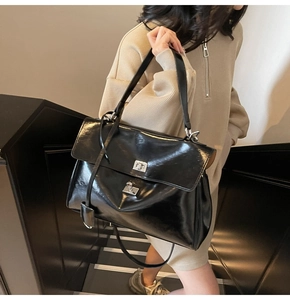 Detail of black glossy tote bag with silver metal swivel lock and sleek flap closure