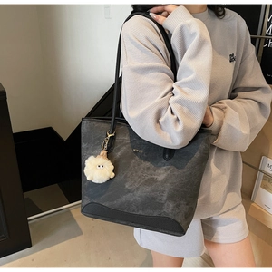 Detail of grey suede tote bag with black textured straps and a fluffy cartoon pendant
