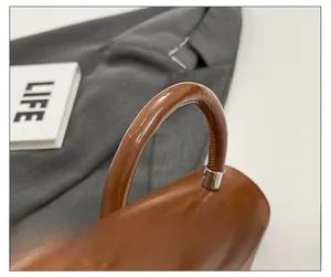 Detail of a brown leather box bag featuring a sturdy curved handle and silver hardware