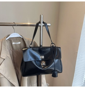 Close-up of black glossy leather tote bag with silver metal rotating lock and double handles