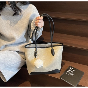 Detail of grey fabric tote bag with black leather trim and white plush charm on stairs