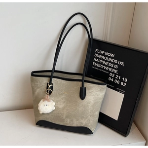 Close-up of olive fabric tote bag with black leather straps and a white fuzzy monster charm