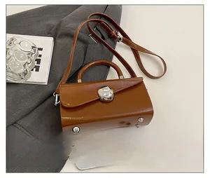 Detail of brown glossy leather crossbody bag with silver clasp and metal feet on bottom