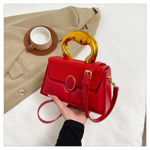 Detail of red leather bag with golden circular metal handle and woven texture panel