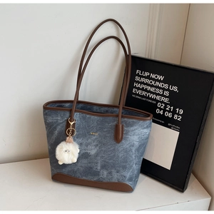 Detail of blue denim tote bag with brown leather trim and soft white pompom keychain