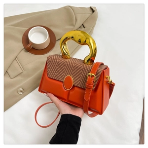 Detail of orange leather box bag featuring a herringbone fabric flap and gold metal handle