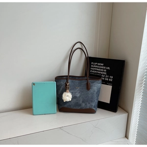 Detail of vintage denim tote bag with leather trim and plush charm beside tablet